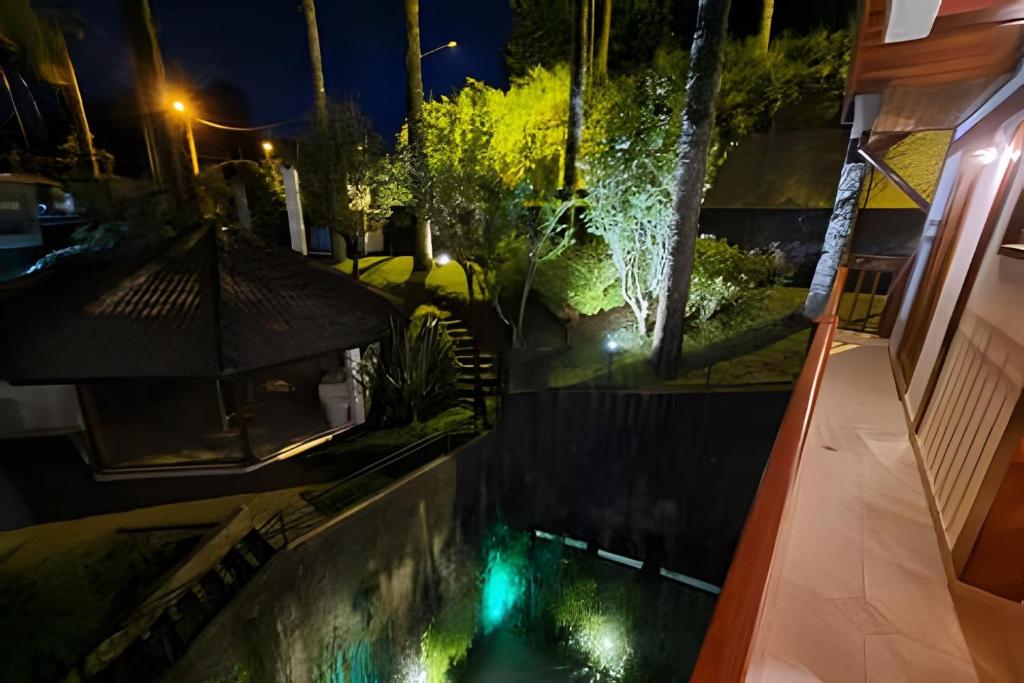 a swimming pool with an umbrella next to a house at night at Apartamentos Centrinho Capivari - Recanto Boticário in Campos do Jordão