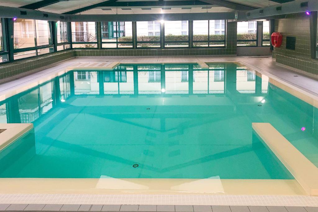 une grande piscine avec de l'eau bleue dans un immeuble dans l'établissement Cosy Home / Disney / Val d'Europe / Paris, à Serris