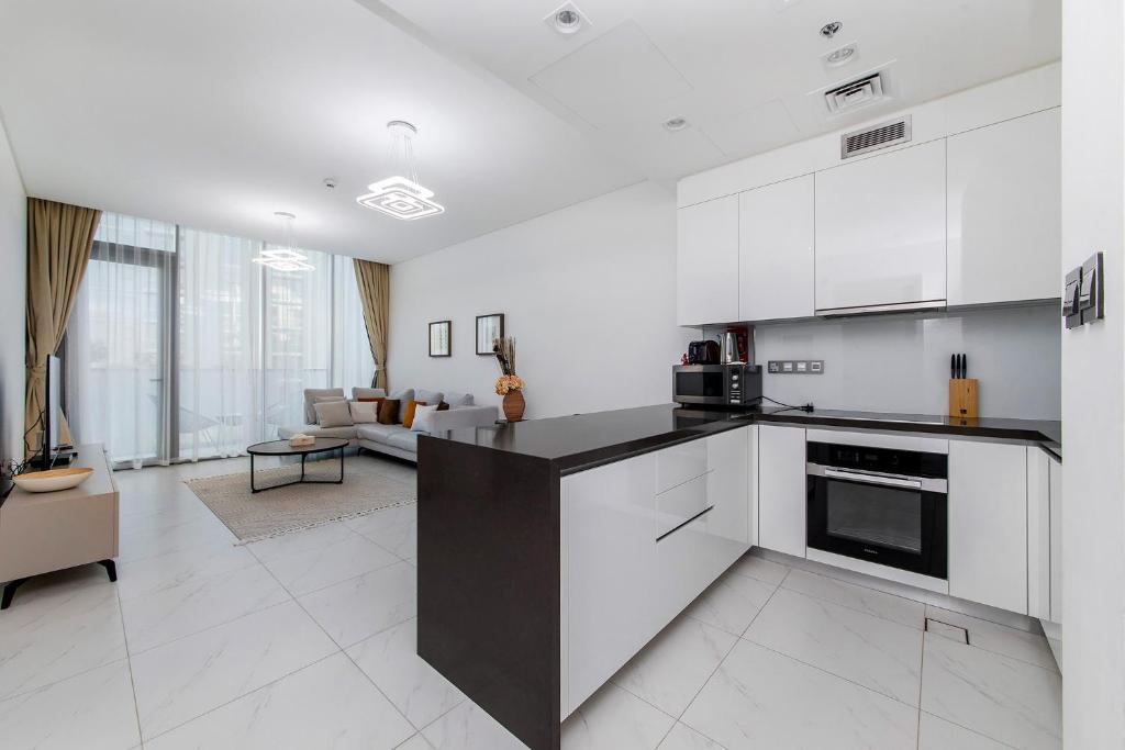 a kitchen with white cabinets and a living room at Aesthetic 1Br Chrystal Lagoon in Dubai