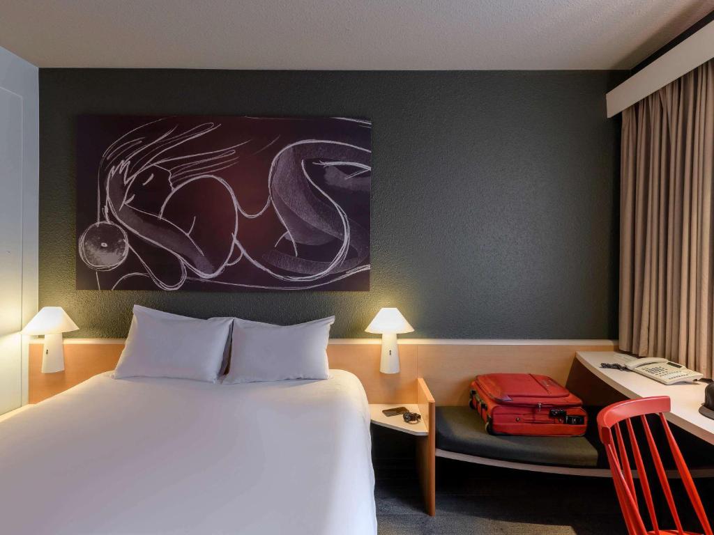 a hotel room with a bed and a desk with a red chair at ibis München Parkstadt Schwabing in Munich