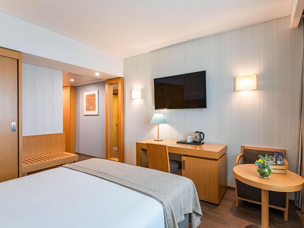 a bedroom with a bed and a desk and a tv at Mercure Lisboa Almada in Almada