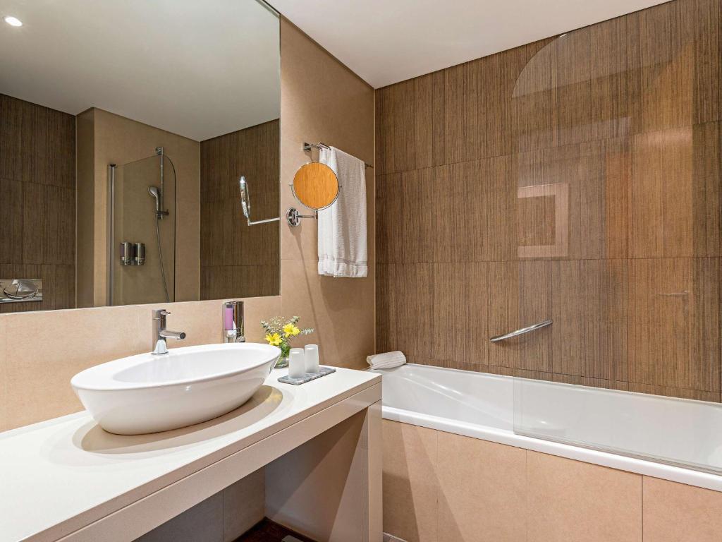 a bathroom with a white sink and a bath tub at Mercure Lisboa Almada in Almada