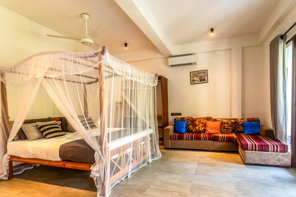 a bedroom with a canopy bed and a couch at 18 Villa in Hikkaduwa