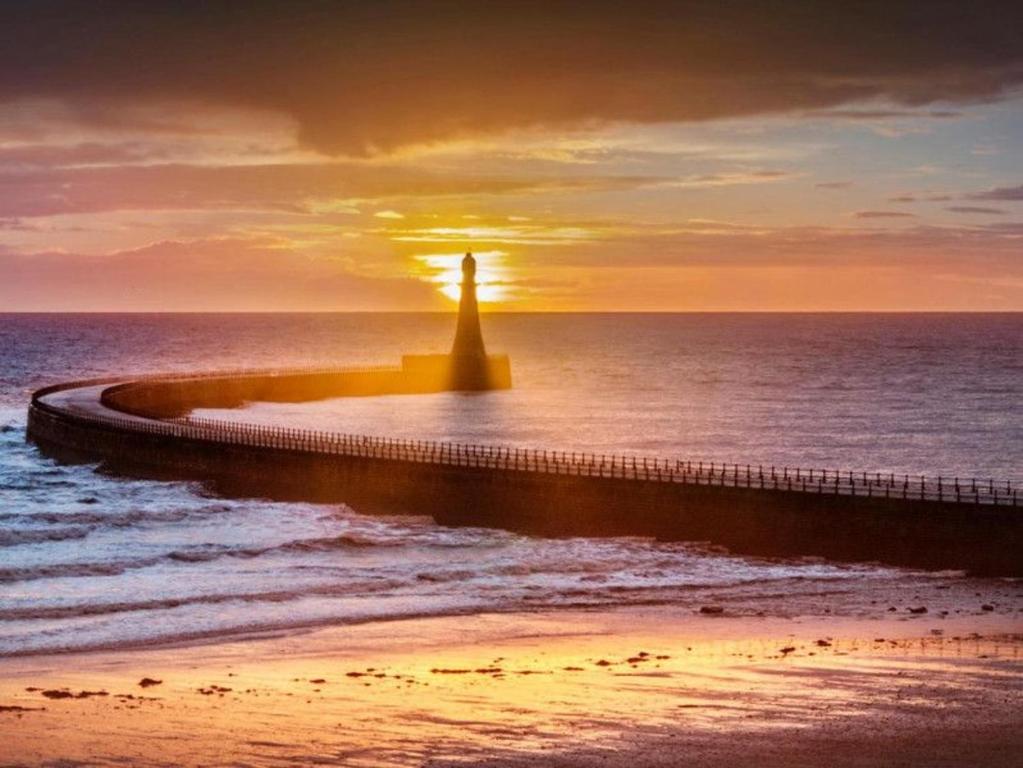 a lighthouse on the beach with the sunset in the background at A&A Luxury Stay Rosedale St - Chic, Modern, City Centre, Neon Decor in Sunderland