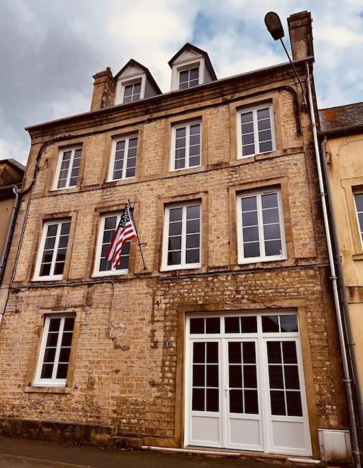 un ancien bâtiment en brique arborant un drapeau américain. dans l'établissement Maison pour 10 personnes max en plein centre de Ste Mère Eglise, à Sainte-Mère-Église