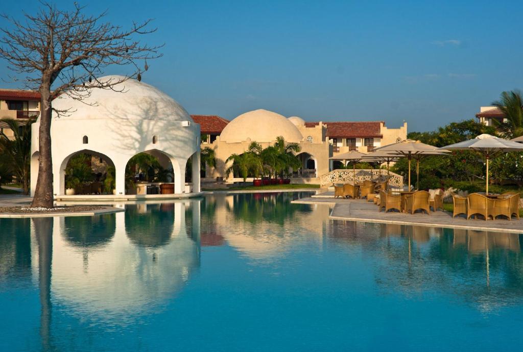 a pool of water in a resort with tables and umbrellas at Swahili Beach in Diani Beach