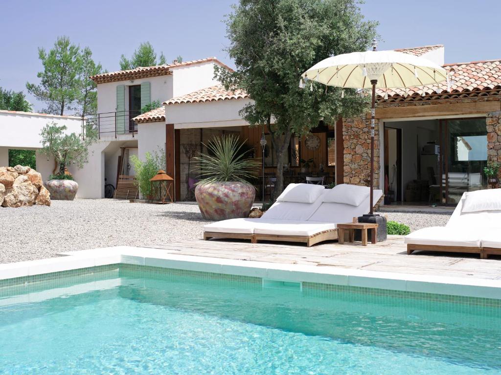 a swimming pool with chairs and an umbrella next to a house at Le Clos Des Cambres in Les Arcs sur Argens