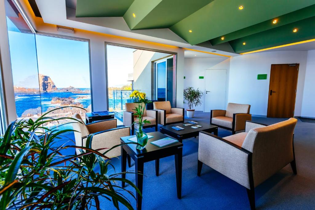 a living room with chairs and tables and windows at Aqua Natura Madeira in Porto Moniz