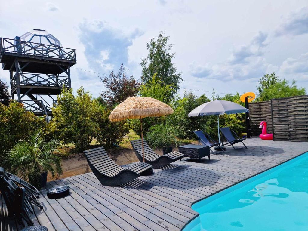 a deck with chairs and umbrellas next to a swimming pool at Kopuła glampingowa Forest in Krzesimów