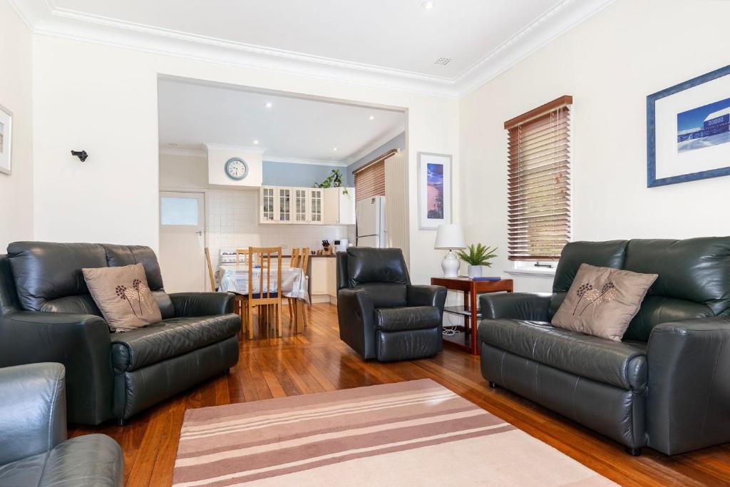 a living room with black leather furniture and a kitchen at Park Rise Cottage in Busselton