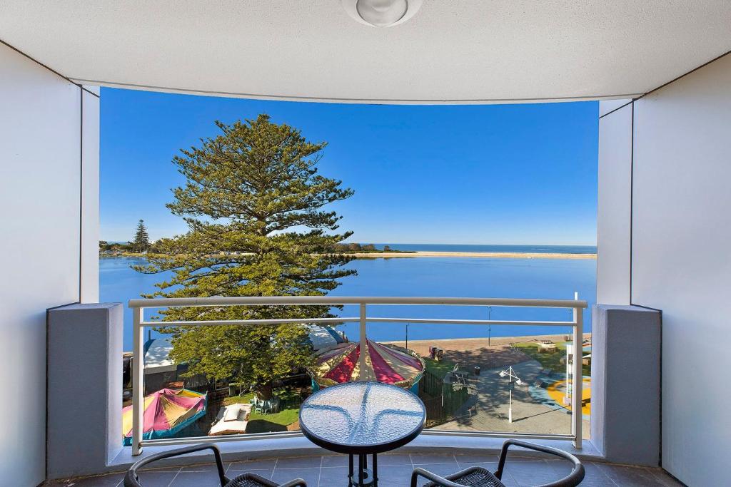 balcón con vistas a un árbol y al agua en The Entrance Waterfont Apartment 303, en The Entrance