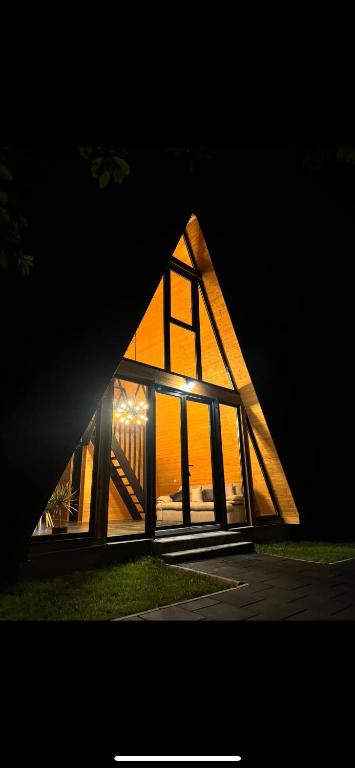 a triangular house with glass windows at night at Nemes Chalet A Frame in Văleni
