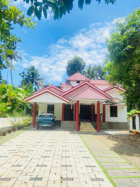 a pink and white house with a driveway at Mampilly Guest House in Kottayam