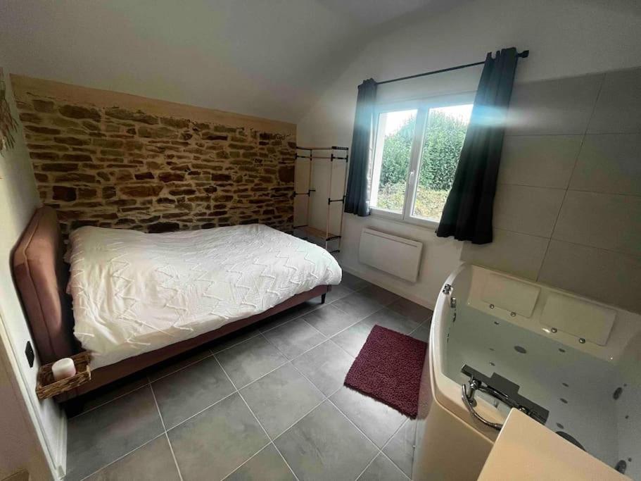 a bedroom with a bed and a brick wall at Gîte en pierre avec baignoire balnéo in Plonéour-Lanvern