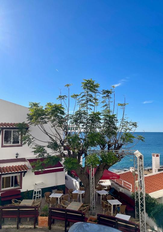 a building with tables and a tree next to the ocean at Casa Luz in Luz