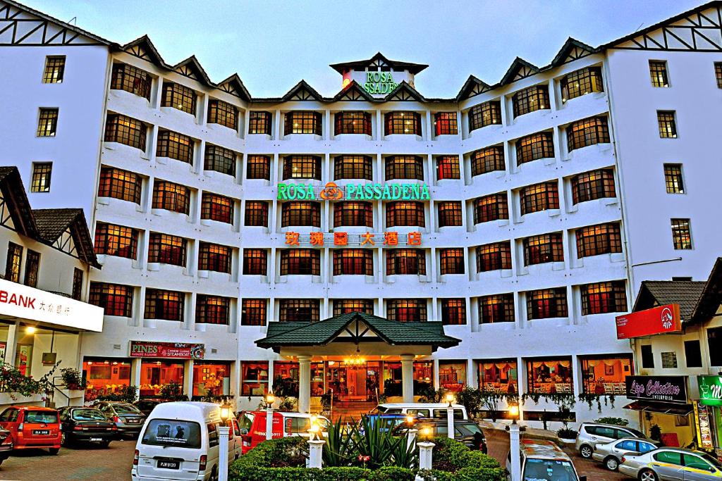 un grand bâtiment blanc avec des voitures garées dans un parking dans l'établissement Hotel Rosa Passadena, à Cameron Highlands