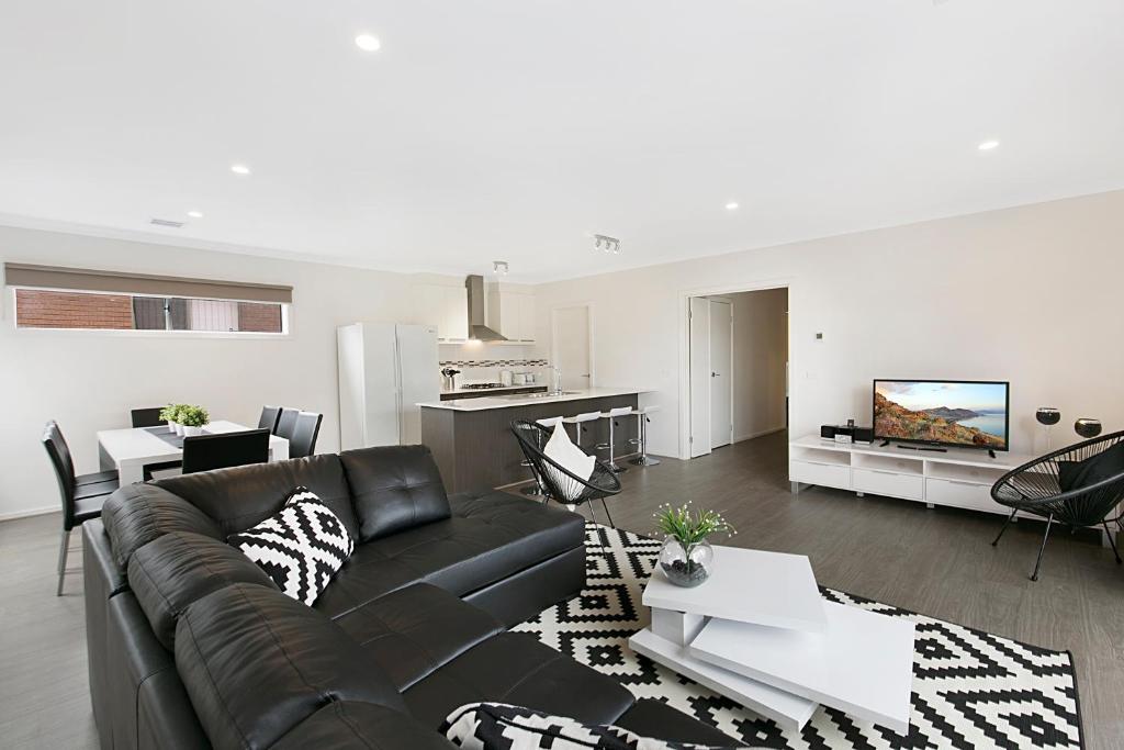 a living room with a black leather couch and a tv at Palm Grove Beach House Dromana in Dromana