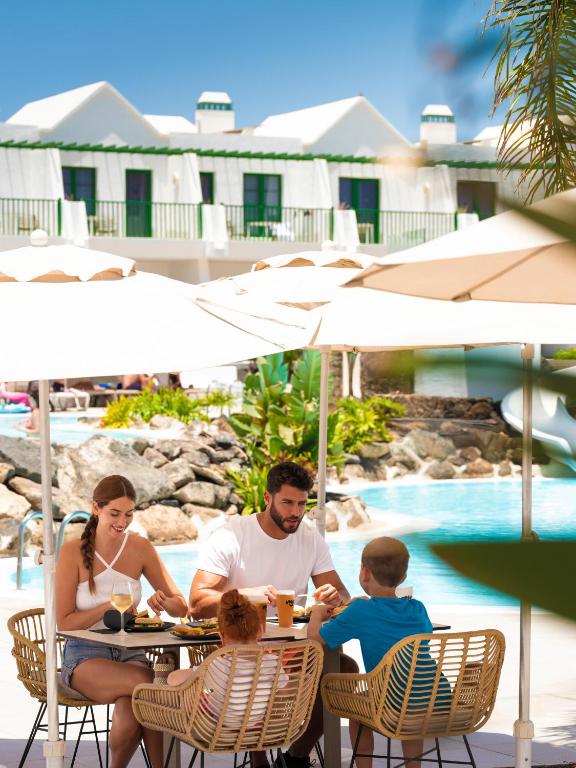 a family sitting at a table in front of a pool at MYND Yaiza in Playa Blanca