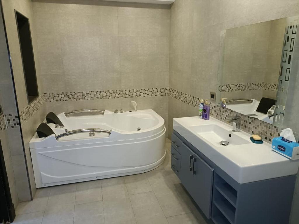 ein Badezimmer mit Badewanne, Waschbecken und Spiegel in der Unterkunft Villa Grand residence Auc شارع ال 90 in Kairo