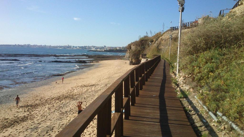 un paseo marítimo que conduce a una playa con gente en ella en PRAIA DAS AVENCAS Apt junto ao mar com estacionamento e AC en Parede