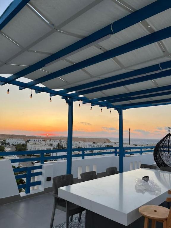 a white table and chairs on a balcony with the sunset at Spacious 3BR Apartment w Rooftop Terrace Jacuzzi in Ras Elhekma