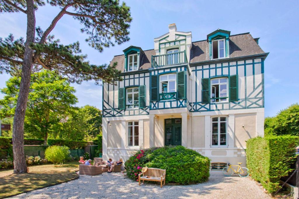 une maison avec des volets verts et des personnes assises devant elle dans l'établissement La Villa Chloé - Proche Plage - Face Au Royal - Deauville, à Deauville