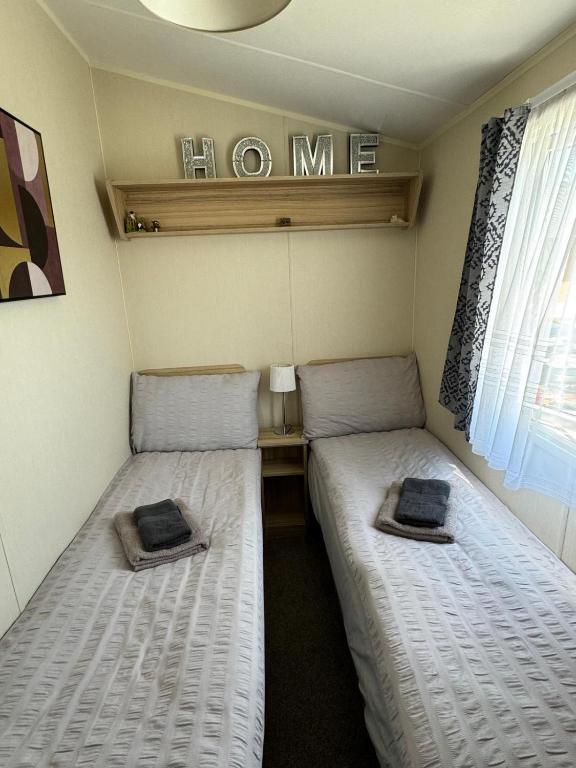 two twin beds in a small room with a window at Comfy Cosy Caravan_Romney Sands in Littlestone-on-Sea