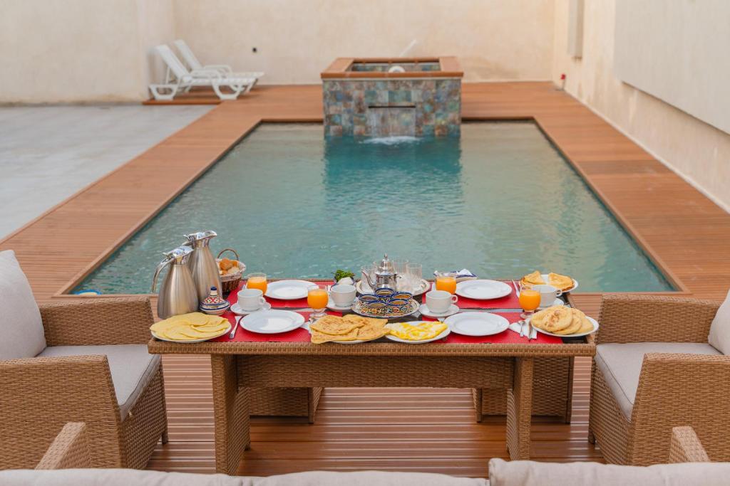 a table with food and drinks in front of a swimming pool at Villa Sable de Mirleft Luxury Apartment in Mirleft