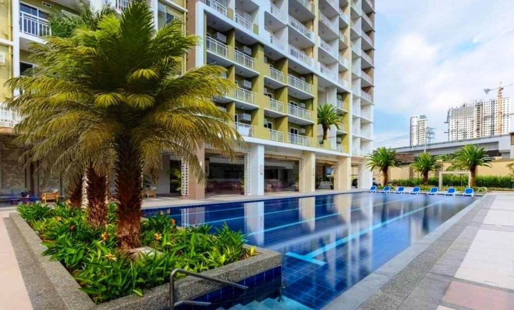 a palm tree in front of a building with a swimming pool at Cuddle & Cradle Staycation at The Celandine in Manila