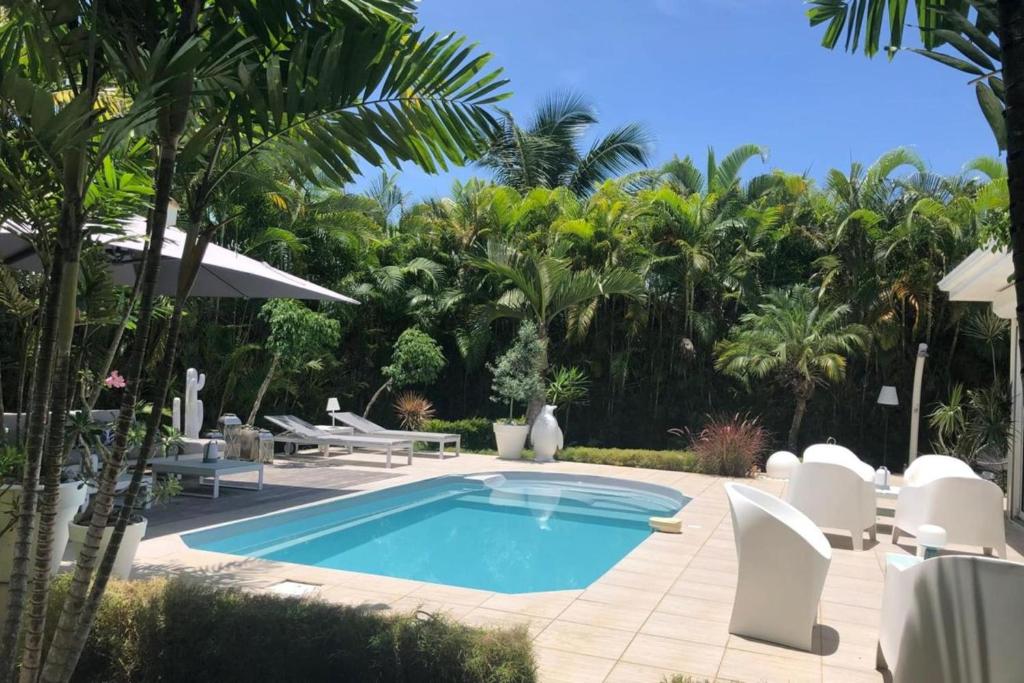 une piscine avec des chaises blanches et un complexe hôtelier dans l'établissement Villa Cava, à Baie-Mahault