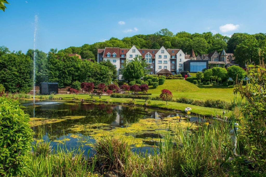 a garden with a pond and houses in the background at DoubleTree by Hilton Bristol South - Cadbury House in Yatton