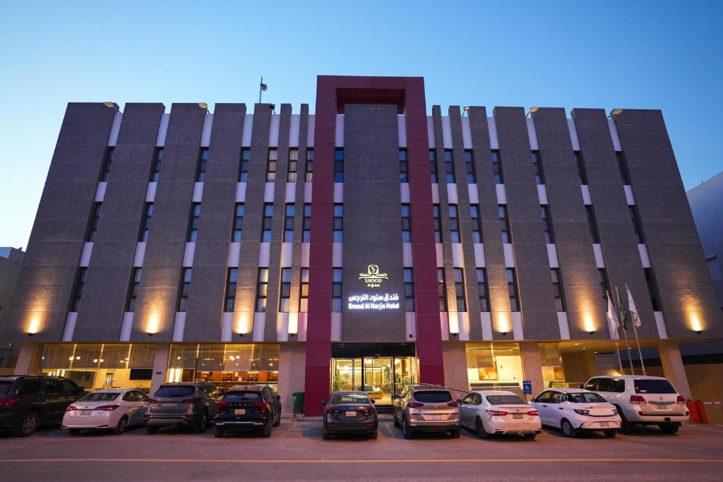 a building with cars parked in a parking lot at Snood Al Narjis Hotel in Riyadh