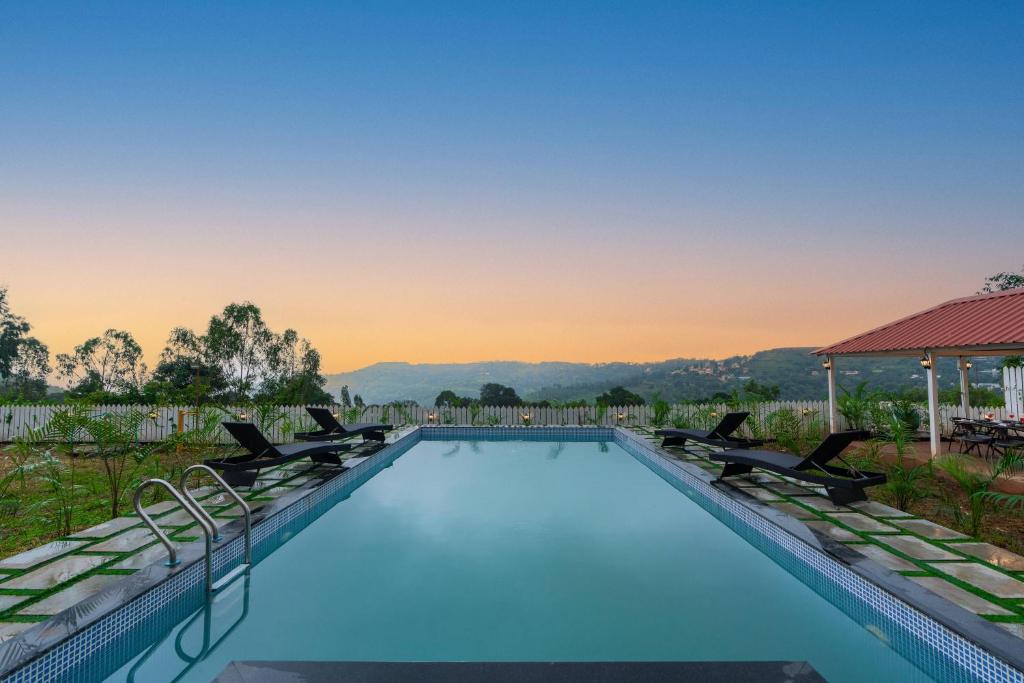 a swimming pool with chairs and a sunset in the background at EKOSTAY Gold - White Swan Villa 6BHK in Panchgani