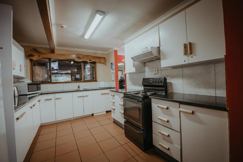 una cucina con armadi bianchi e un forno a piano cottura nero di Storms River Forest Lodge a Stormsrivier