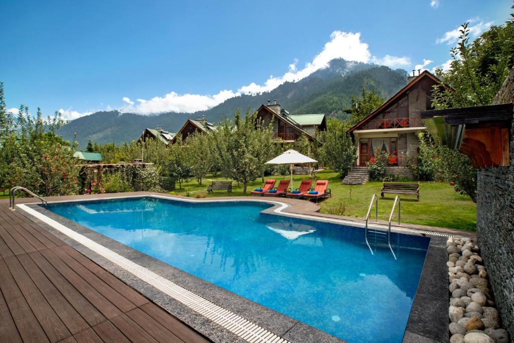 a swimming pool with a house and mountains in the background at Larisa Resort Manali in Manāli