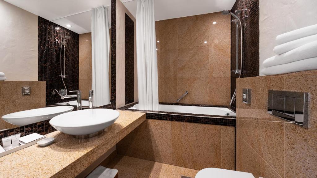 Marble bathroom with vessel sink, bathtub, glass shower, handheld shower, mosaic tile border and stacked towels at Rixwell Collection Savoy Boutique Hotel in Tallinn