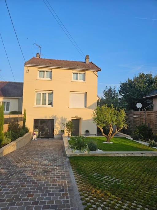 une grande maison jaune avec une allée en briques dans l'établissement Belle Maison avec Jardin, à Pierrelaye