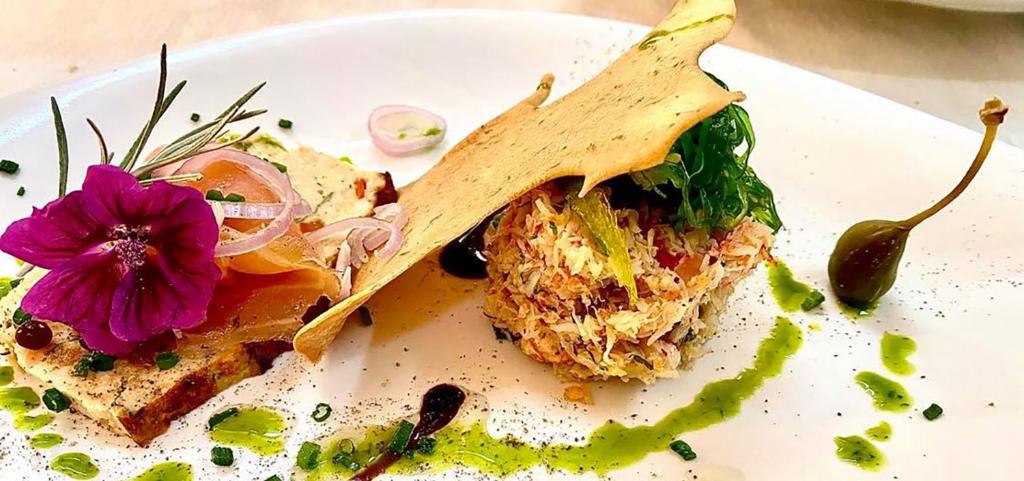 a white plate with a sandwich and a purple flower at Hotel Restaurant Le Cigalon in Waldbillig