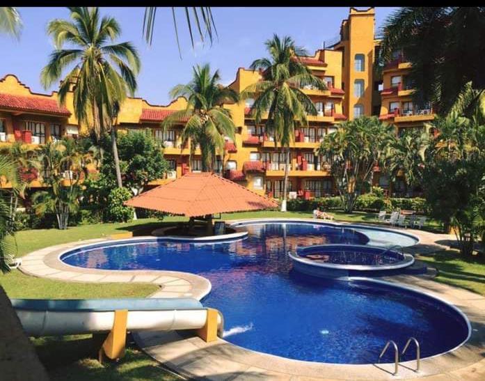 a swimming pool with an umbrella in front of a building at Suit Junior Emano 410 in Ixtapa