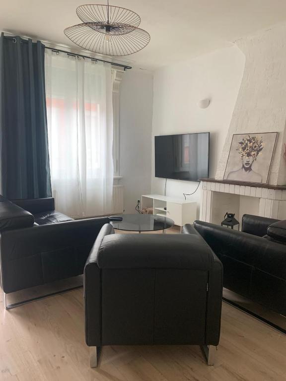 - un salon avec deux canapés noirs et une télévision dans l'établissement Jolie Maison de ville, à Valenciennes