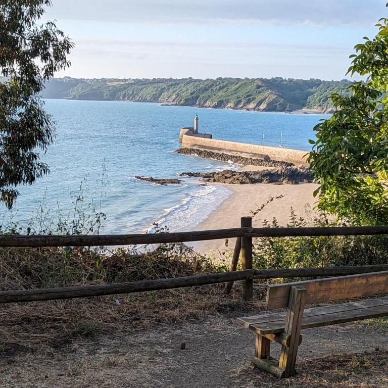 un banc en bois assis sur une plage à côté d'une clôture dans l'établissement Maison à Binic, à Gicquel