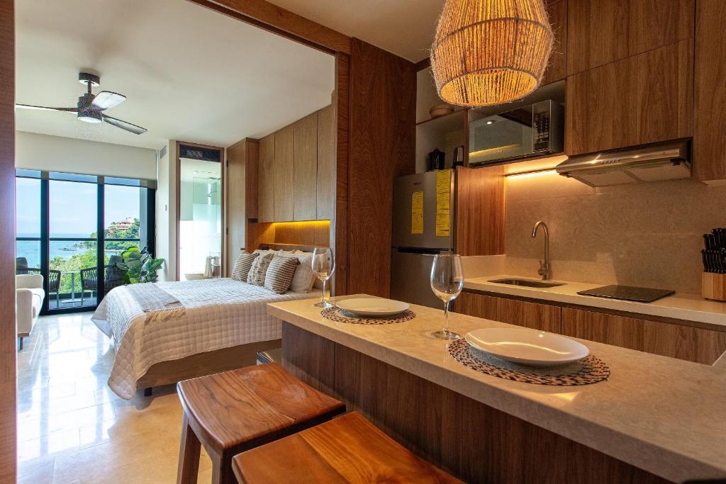 a room with a bed and a kitchen with glasses on a counter at Hermoso Estudio frente al mar, Zantamar 304 in Cruz de Huanacaxtle