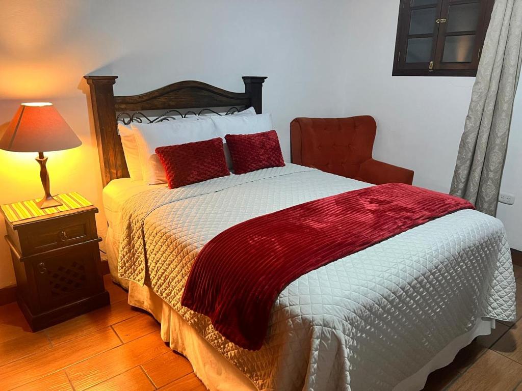 Un dormitorio con una cama con almohadas rojas y una lámpara. en Villa de Los Ángeles, en Antigua Guatemala