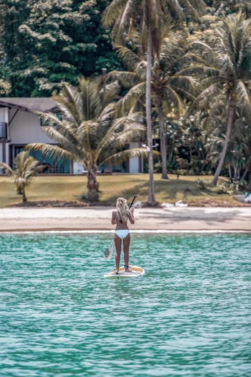 a girl is standing on a surfboard in the water at Barcelo Coconut Island, Phuket in Phuket Town