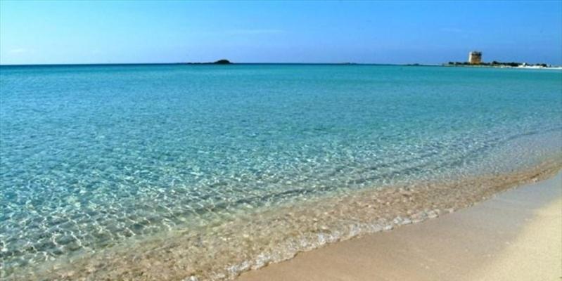 a beach with blue water and a lighthouse in the background at Casa Vacanze San Giacomo Comfort Apartment in Centro a pochi passi dal Mare in Barletta
