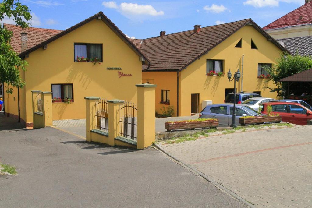 un bâtiment jaune avec des voitures garées dans un parking dans l'établissement Pensiunea Blanca, à Reghin