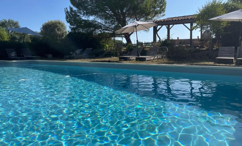 a swimming pool with blue water and umbrellas at Hameau du HOUR - Chambres d'Hôtes et Gîtes dans le Gers in Béraut