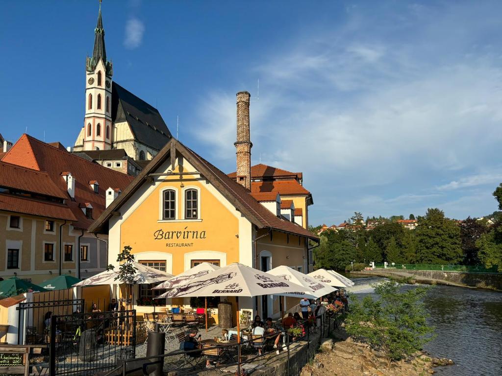 a building with tables and umbrellas next to a river at Boutique Hotel Barvírna in Český Krumlov