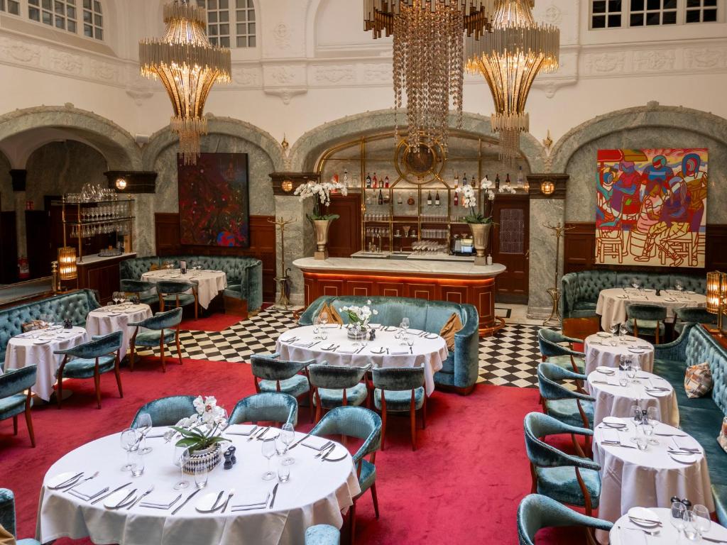 a restaurant with white tables and chairs and a chandelier at Bank Hotel, a Member of Small Luxury Hotels in Stockholm