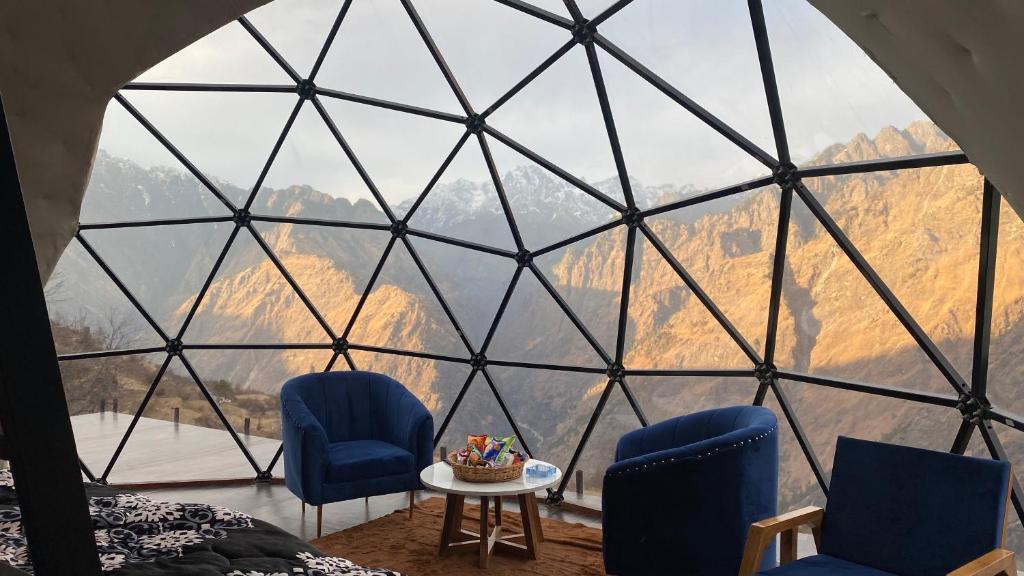 a room with a view of the mountains through a glass window at We Are Made Of Stories in Joshīmath